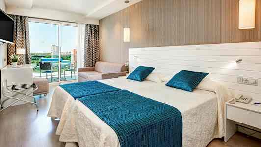 Hotellrom med to senger, en sofa og en glassbalkong. (AI-generert tekst)