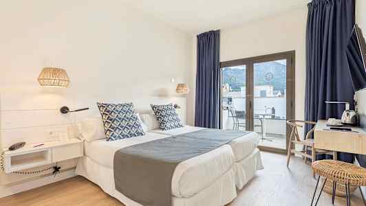 Et hotellrom med to enkeltsenger, blå dekorputer, skrivebord og en balkong med utsikt. (AI-generert tekst)