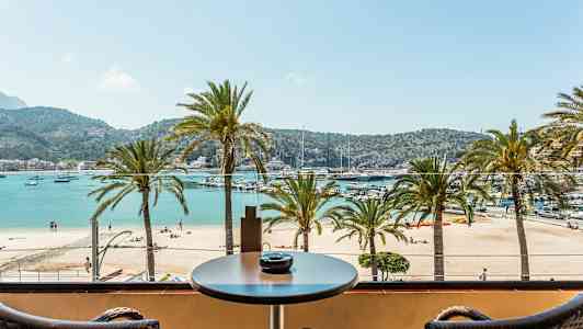 Utsikt fra en balkong mot en strand med palmer og hav på en solrik dag. (AI-generert tekst)