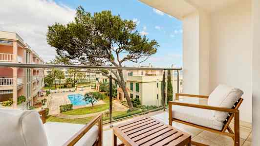 Utsikt fra en balkong med sittemøbler, mot en indre gårdsplass med basseng og omkringliggende bygninger. (AI-generert tekst)