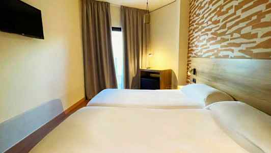 To enkeltsenger på et hotellrom med et mønstret hodegjerde og en TV på veggen. (AI-generert tekst)