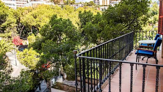 Balkong med bord og stoler med utsikt til frodig vegetasjon. (AI-generert tekst)