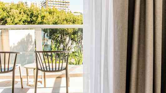 To stoler og et bord på en balkong med grøntområder og bygninger i bakgrunnen. (AI-generert tekst)