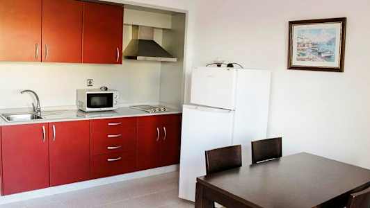 Et kjøkken med røde skap, et kjøleskap og en spiseplass med bord og stoler. (AI-generert tekst)