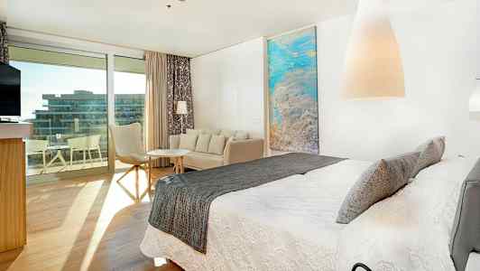 Moderne hotellrom med stor seng, sittegruppe og utgang til balkong. (AI-generert tekst)