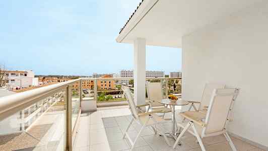 En balkong med bord og stoler samt utsikt over omkringliggende bygninger. (AI-generert tekst)