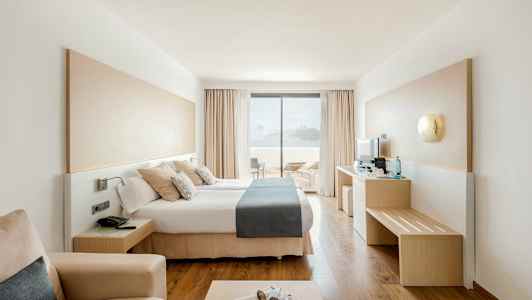 Moderne hotellrom med dobbeltseng og utsikt mot terrasse og hav. (AI-generert tekst)