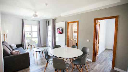 En stue med grå sofa, spisebord med stoler, og en TV på veggen. (AI-generert tekst)