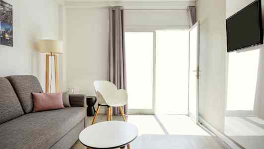 En lys og moderne innredet stue med grå sofa, en hvit stol og et rundt sofabord. (AI-generert tekst)