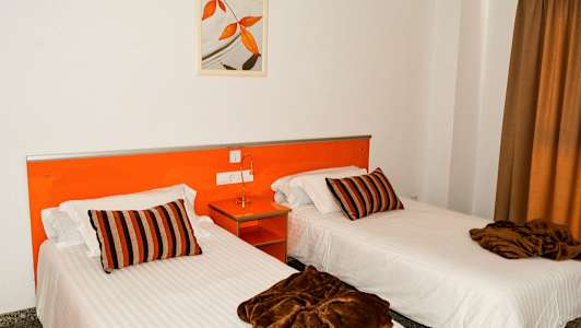 To enkeltsenger med hvite laken, brune tepper og stripete puter i et rom med oransje interiør. (AI-generert tekst)