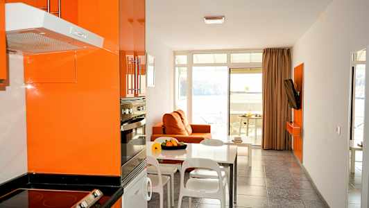 Moderne kjøkken og stue med oransje innredning og utsikt mot havet. (AI-generert tekst)