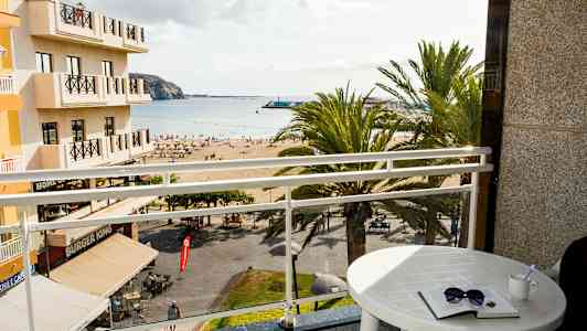 Utsikt fra et hotellrom med en balkong mot en strand og havet. (AI-generert tekst)