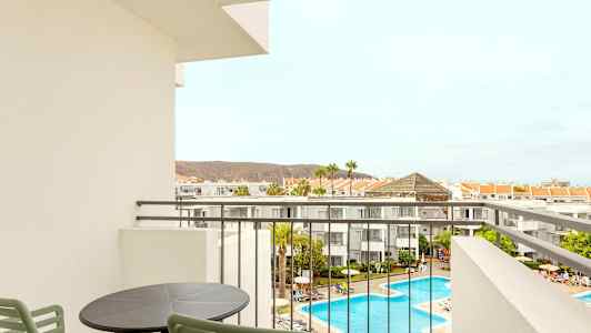 Utsikt fra en balkong over hotellområdet med basseng og omkringliggende bygninger. (AI-generert tekst)