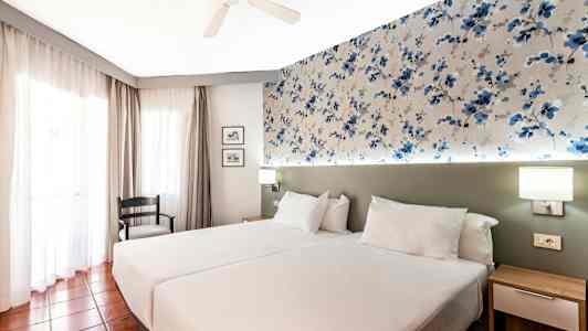 Et hotellrom med to enkeltsenger og mønstret veggdekorasjon. (AI-generert tekst)