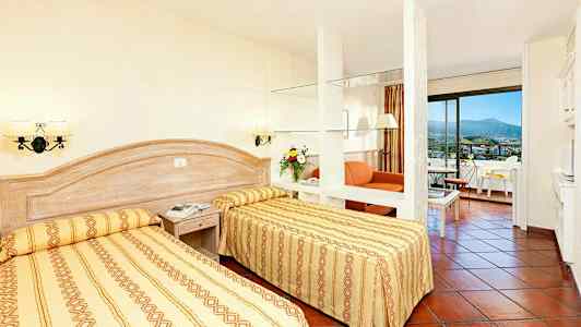 Et hotellrom med to enkeltsenger, en sittegruppe og balkong. (AI-generert tekst)