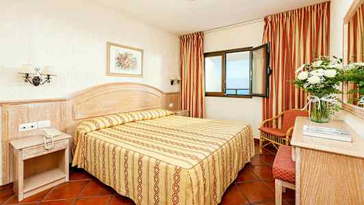 Et hotellrom med dobbeltseng, nattbord og vindu med havutsikt. (AI-generert tekst)