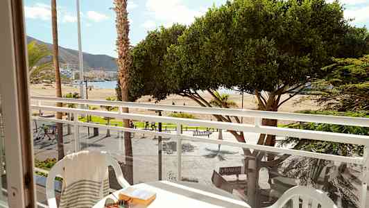 Utsikt fra en balkong mot en strand med palmer og trær. (AI-generert tekst)