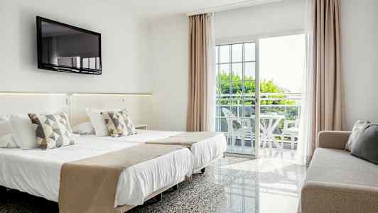 Hotellrom med dobbeltseng, sofa, veggmontert TV og balkong med møbler. (AI-generert tekst)