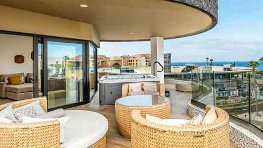 En romslig balkong med sittemøbler og et boblebad, utsikt over bygninger og havet. (AI-generert tekst)