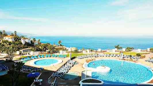 Bilde av et hotell med bassengområde i forgrunnen og havutsikt i bakgrunnen. (AI-generert tekst)