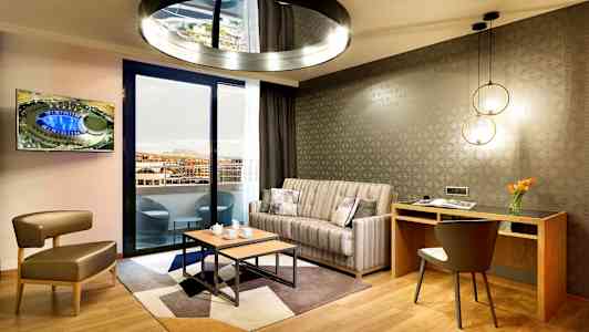 Moderne stue med sofagruppe, et skrivebord og utsikt mot en balkong. (AI-generert tekst)