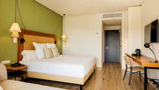 Hotellrom med en bred seng, skrivebord og grønn vegg. (AI-generert tekst)