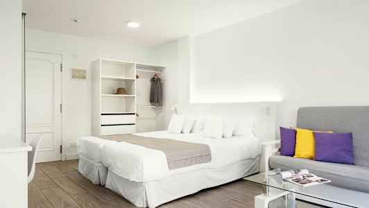 Et lyst hotellrom med en dobbeltseng, en sofa og et garderobeskap. (AI-generert tekst)