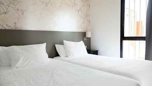 Et hotellrom med to enkeltsenger og et nattbord.  (AI-generert tekst)