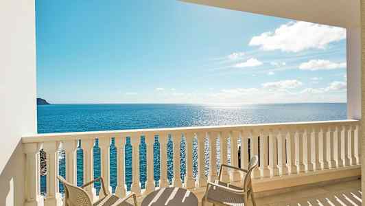 Utsikt fra en balkong med bord og stoler mot havet. (AI-generert tekst)