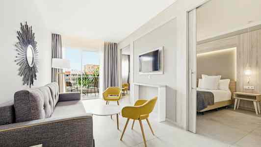 Lyst og moderne hotellrom med sittegruppe, soverom og balkong. (AI-generert tekst)