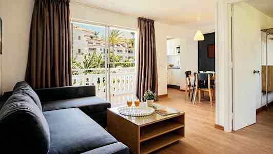 En stue med mørk sofa, et sofabord og utsikt over en balkong med grønne omgivelser. (AI-generert tekst)