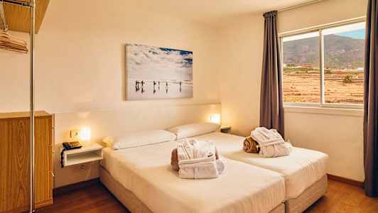 Et lyst hotellrom med en dobbeltseng, vindu med utsikt over landskapet og et veggmaleri over sengen. (AI-generert tekst)