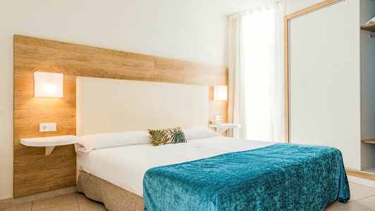 Moderne hotellrom med en stor seng dekket med et blått teppe og vegglamper på sidene. (AI-generert tekst)