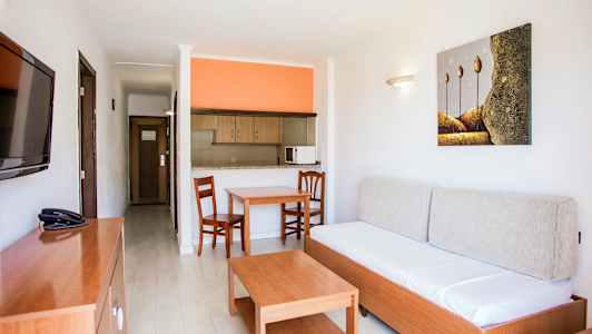 Leilighetsinteriør med en sofa, et bord, to stoler og et åpent kjøkken med oransje vegg. (AI-generert tekst)