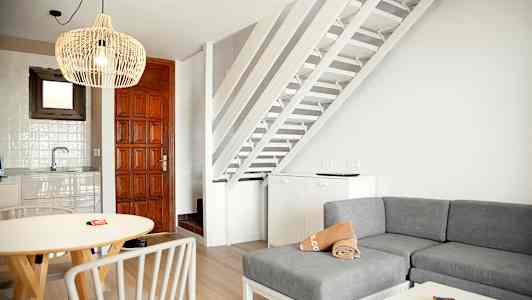 Innendørs visning av stue, kjøkkenområde og trapper med hvit og treinnredning. (AI-generert tekst)