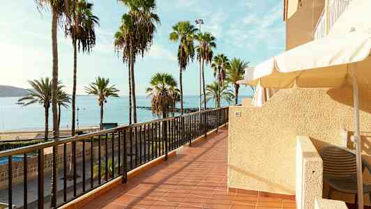 Bilde av en terrasse med utsikt over en strand med palmer og hav. (AI-generert tekst)