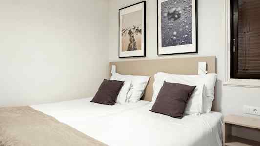 Et soverom med to enkeltsenger, hvite laken, mørke puter og to innrammede bilder på veggen. (AI-generert tekst)