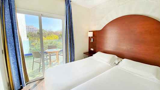 Et hotellrom med to enkeltsenger, en trehodegavl og en balkong med to stoler og et bord utenfor. (AI-generert tekst)