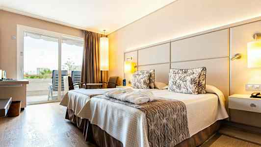 Hotellrom med to senger og interiør i nøytrale toner. Utsikt mot balkong gjennom glassdører. (AI-generert tekst)