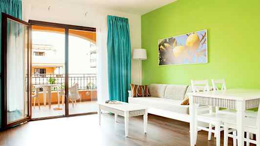 Stue med grønn vegg, hvit sofa, hvite møbler og utsikt mot balkong. (AI-generert tekst)