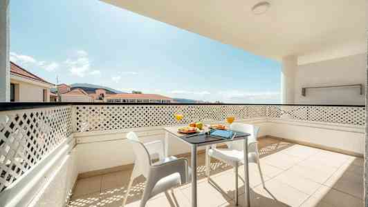 Balkong med bord og stoler samt utsikt over omkringliggende bygninger og fjell. (AI-generert tekst)