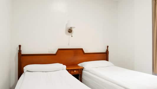 To enkeltsenger med hvite laken og sengegavler av tre står ved siden av hverandre. (AI-generert tekst)