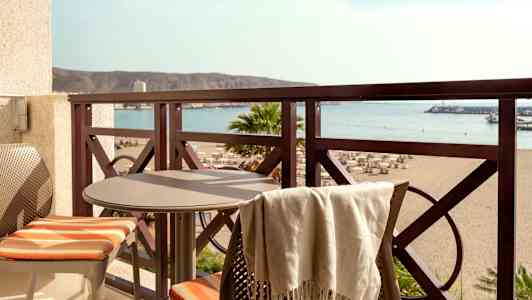 Balkong med bord og to stoler samt utsikt over stranden og havet. (AI-generert tekst)