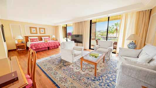 Et hotellrom med en seng, sittemøbler og en balkong med utsikt. (AI-generert tekst)