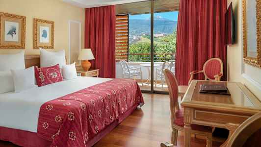 Hotellrom med dobbeltseng, skrivebord, stol og balkong med utsikt mot natur og fjell. (AI-generert tekst)