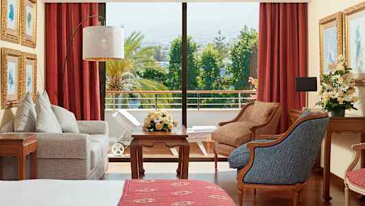 Et hotellrom med møbler, blomster og utsikt over en frodig balkong. (AI-generert tekst)