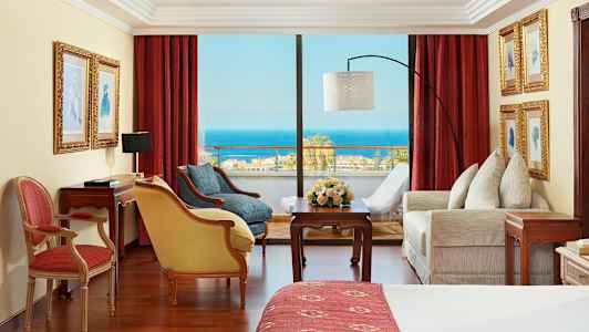 Rom med røde gardiner, møbler og utsikt over havet. (AI-generert tekst)