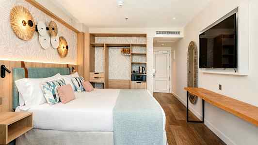 Et moderne hotellrom med en stor seng, innredning i lyse farger og designdetaljer, inkludert en veggdekorasjon og en stor veggmontert TV. (AI-generert tekst)