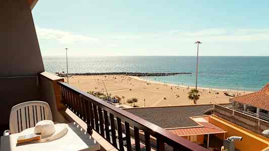 En balkong med utsikt over en sandstrand og havet. (AI-generert tekst)