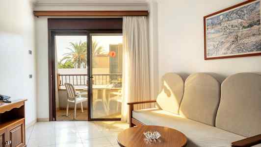 Et hotellrom med sofa, sidebord og en balkong med utsikt. (AI-generert tekst)